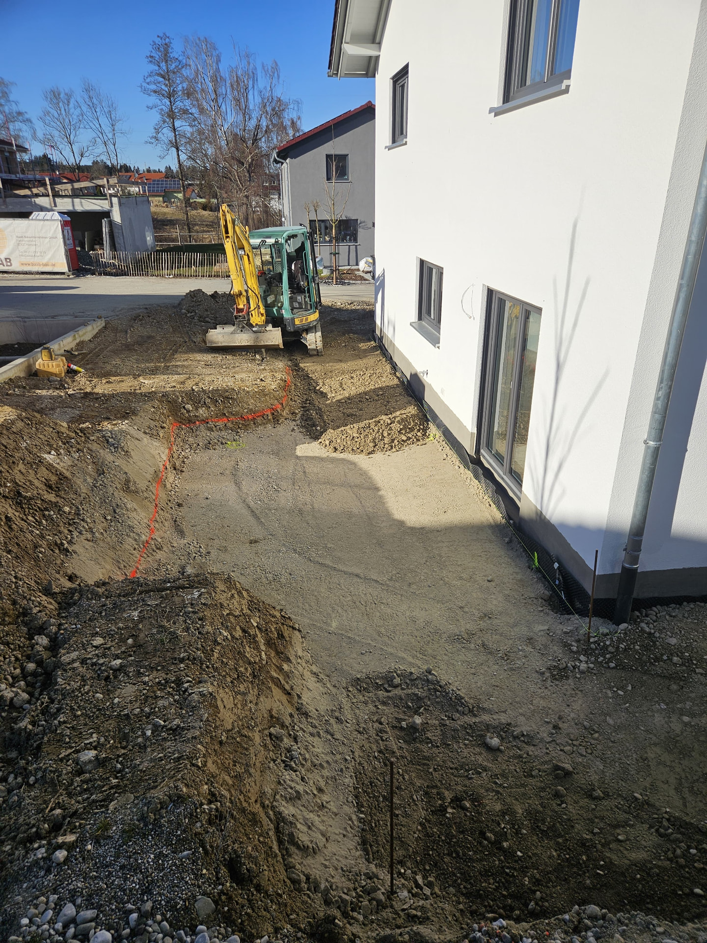 Minibagger bei Erdarbeiten neben einem Wohnhaus mit ausgehobenem Graben